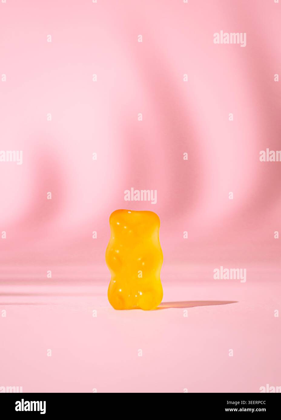 Minimale gelbe gummiartige Bonbons auf rosafarbenem Hintergrund mit kreativem Schatten. Trendiges Gummikonzept. Gelee-Süßigkeiten-Ästhetik. Stockfoto