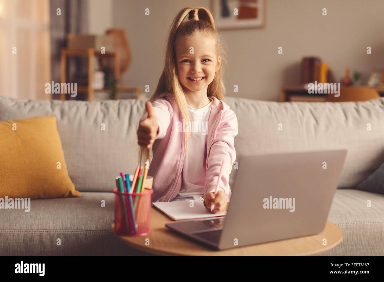 Das Mädchen benutzt Laptop auf der Couch, während es Buntstifte in der Hand hält Stockfoto