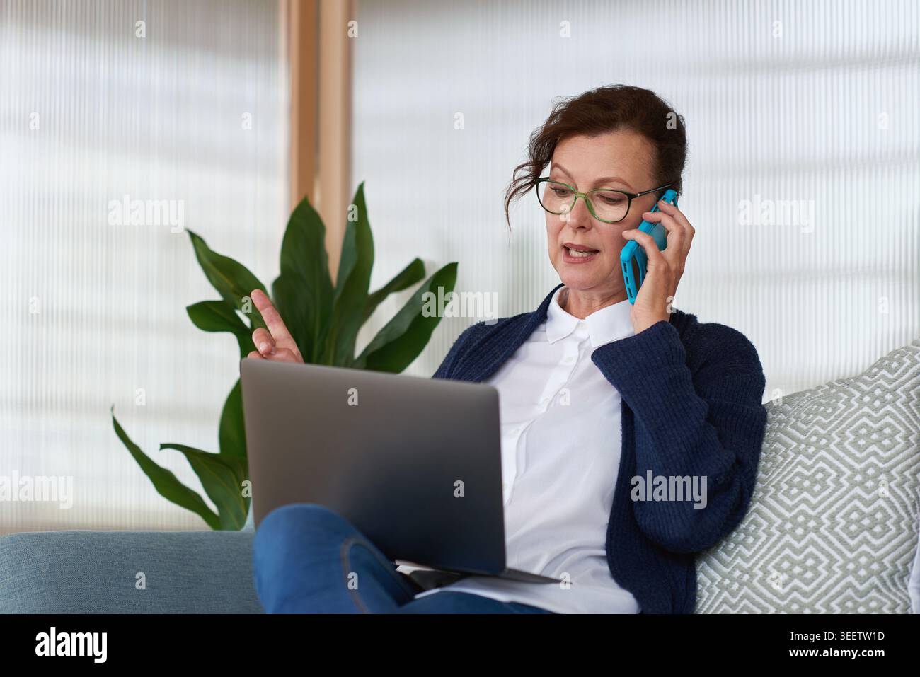 Frau, Laptop und Telefonanruf auf Sofa für Fernarbeit von zu Hause, Brille oder Diskussion im Wohnzimmer. Reifer Mensch, virtueller Assistent und Computer Stockfoto