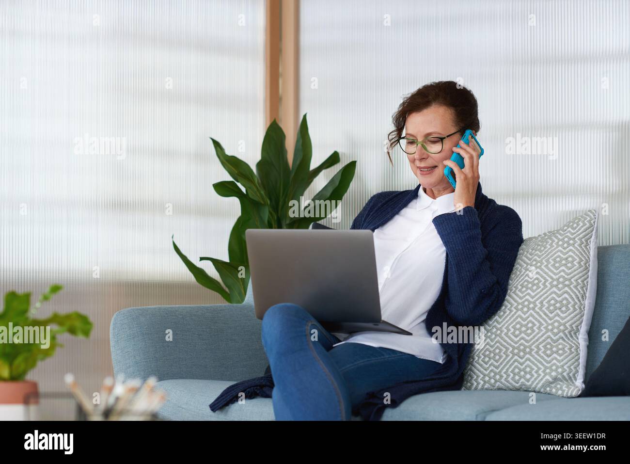 Frau, Laptop und Telefonanruf auf der Couch für Fernarbeit von zu Hause aus, Brille oder Diskussion im Wohnzimmer. Reifer Mensch, virtueller Assistent und Computer Stockfoto