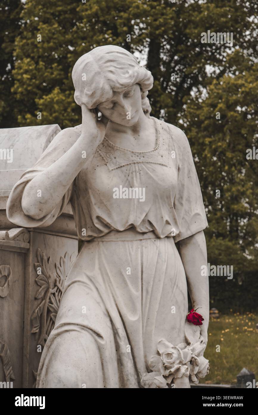 Marmortrauerstatue der trauernden Frau auf dem historischen Friedhof mit Rose- und Blumenschnitzereien Stockfoto