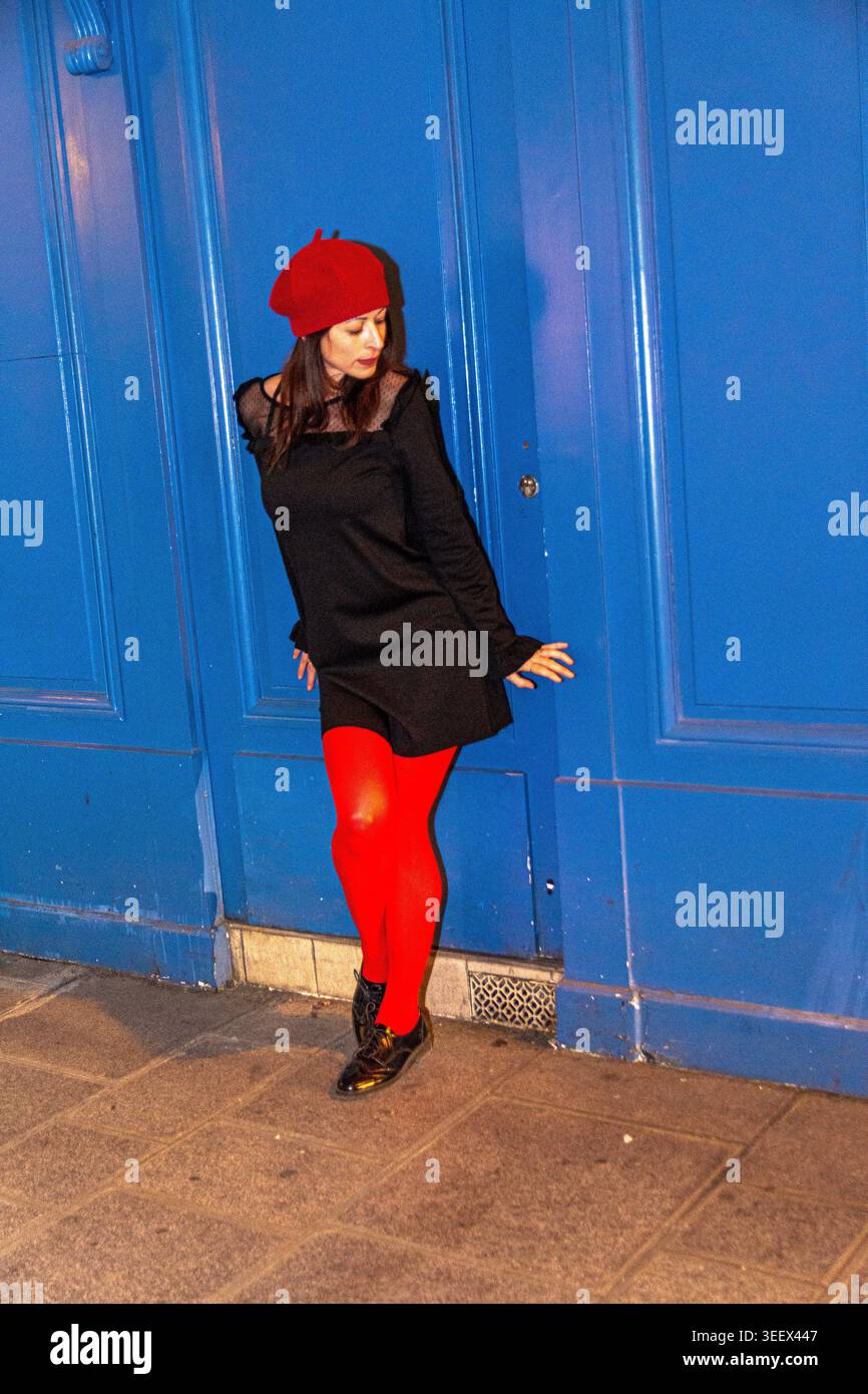 Frau mit roter Baskenmütze und Strumpfhosen, die in urbaner Umgebung posiert Stockfoto