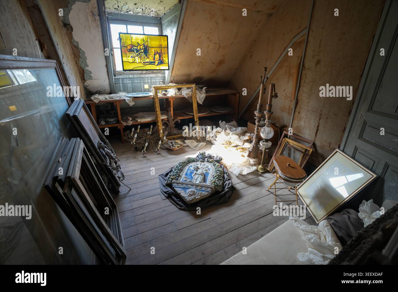 Ein nicht restaurierter Dachboden im Château de Chaumont beherbergt gerahmte Kunstwerke, ein großes skulpturales Reliefemblem und antike Lampen auf Holzdielen Stockfoto