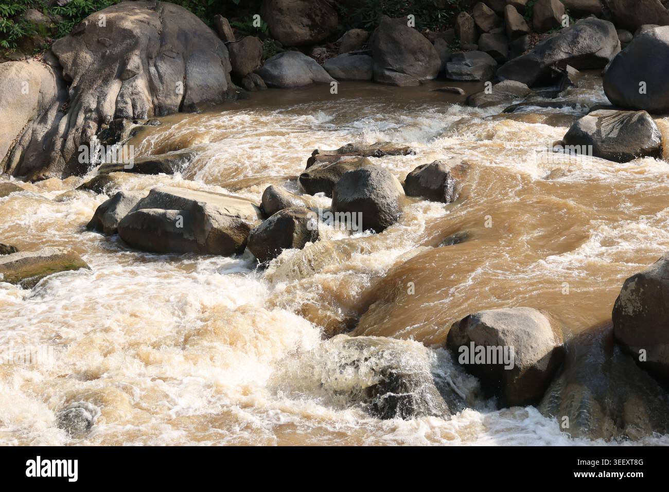 Schlammwasser fließt gewaltig über große Felsen- und Felsformationen und erzeugt einen wilden, chaotischen Fluss, der sich kraftvoll gefährlich und ungefährlich anfühlt Stockfoto