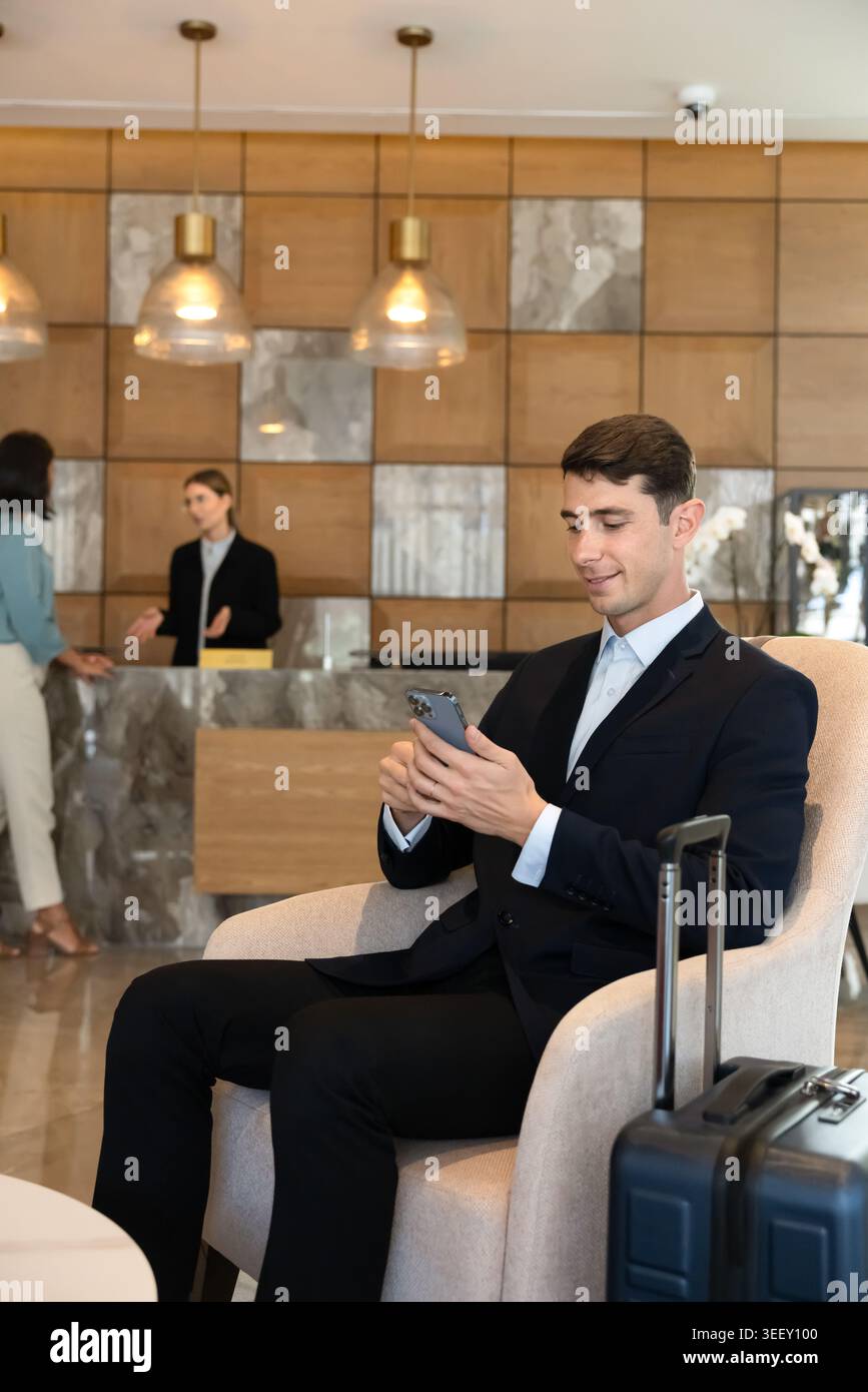 Geschäftsmann sitzt in der Hotellobby mit Smartphone Stockfoto