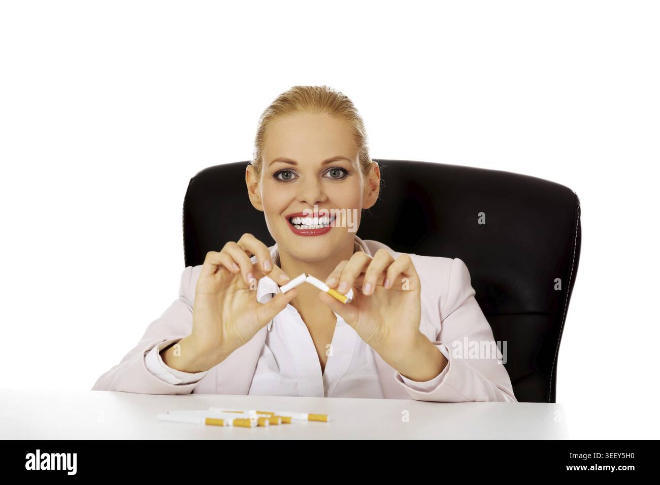 Lächelnde Geschäftsfrau, die hinter dem Schreibtisch sitzt und Zigaretten bricht Stockfoto