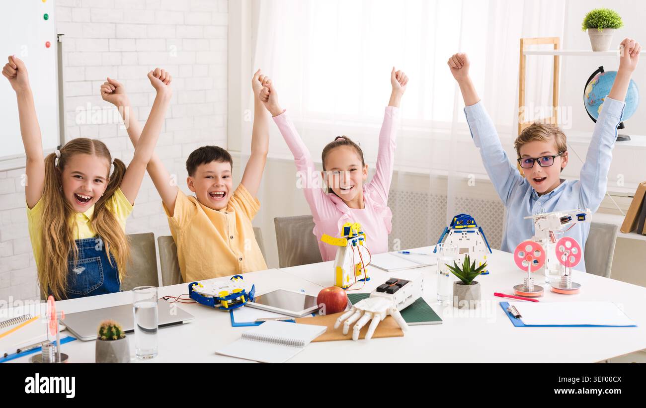 Kinder feiern den Erfolg in einem Robotik-Workshop in einem modernen Klassenzimmer während des Tages Stockfoto