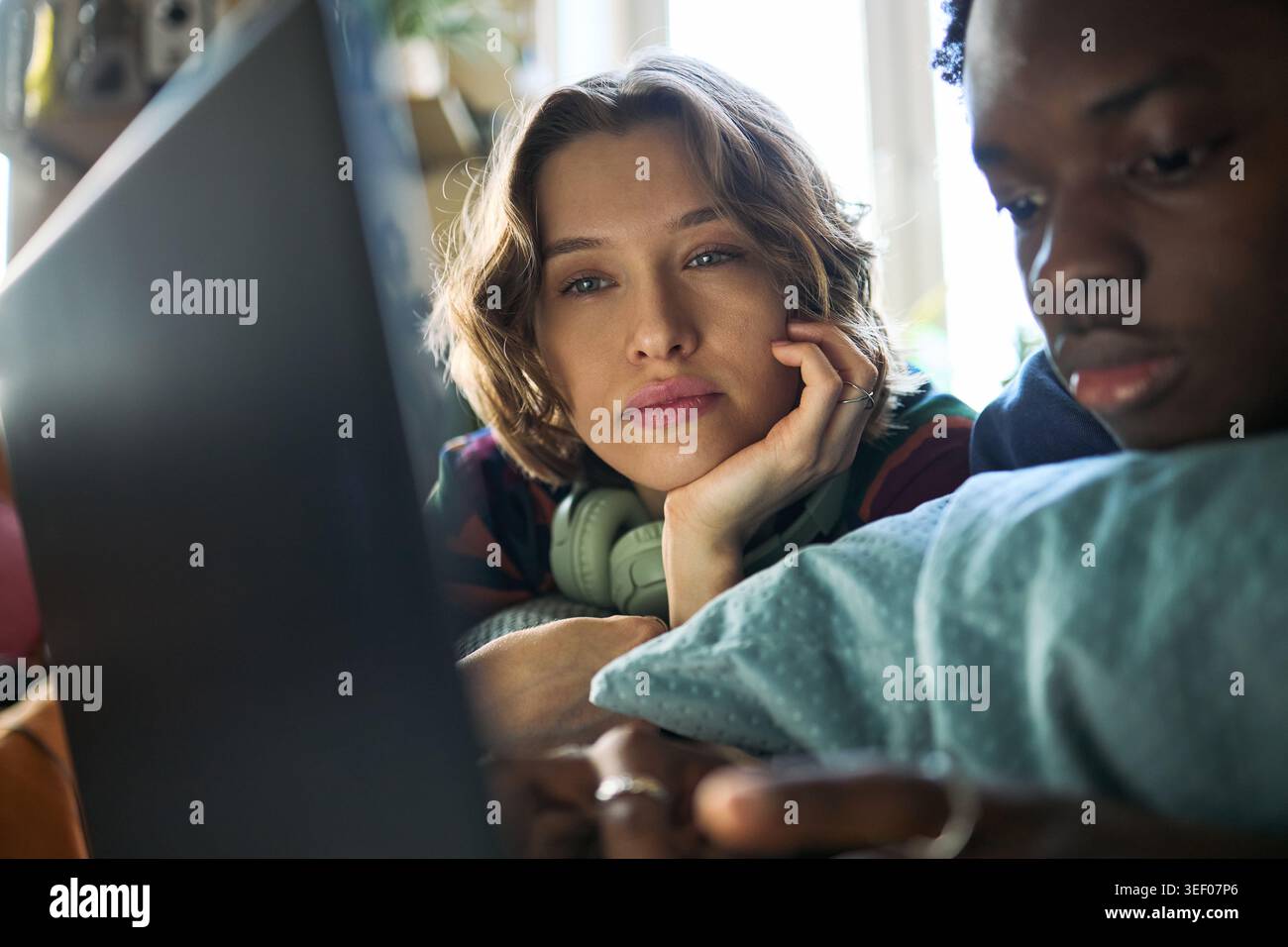 Porträt einer jungen kaukasischen Frau und eines jungen Schwarzen Mannes, die sich zu Hause entspannen und Laptop und Smartphone verwenden, um den digitalen Lebensstil und das Surfen von Inhalten für Tech-Marketing darzustellen Stockfoto