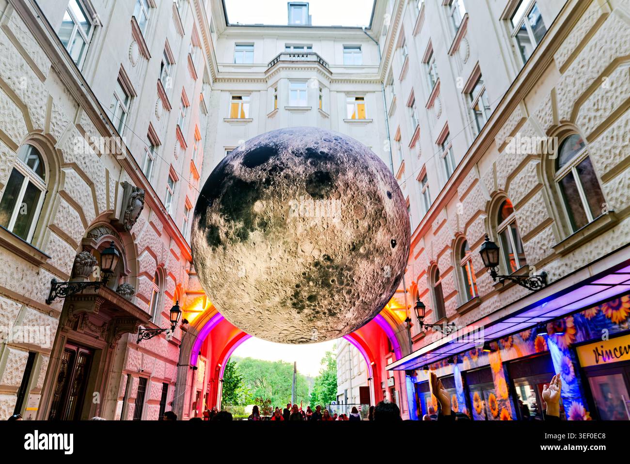 Besucher treffen sich unter einer großen Mondskulptur in Budapest. Die Szene spielt in einem städtischen Innenhof, der von Gebäuden umgeben ist. Stockfoto