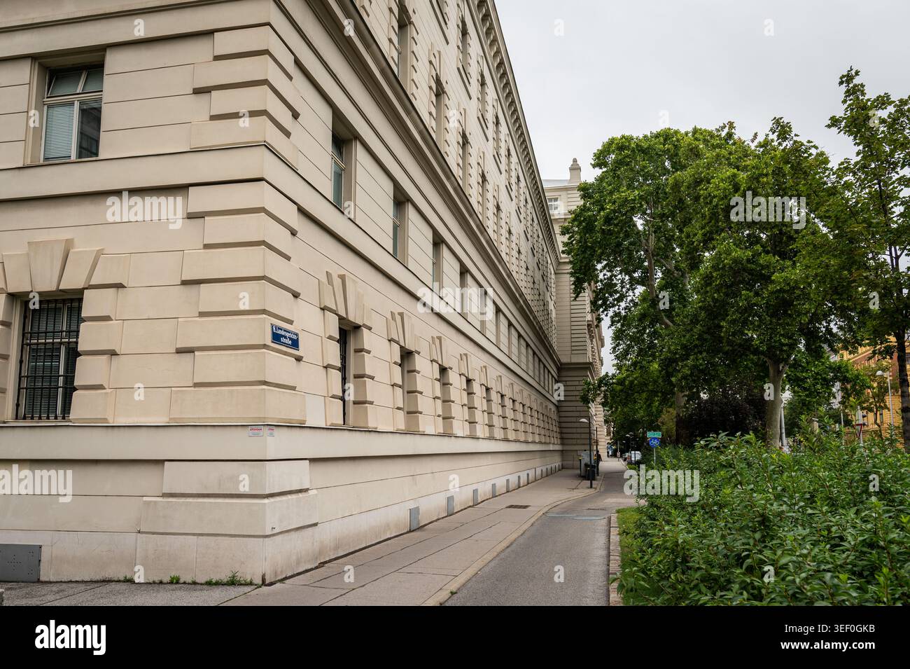 Wien, Österreich - 4. August 2020: Die lange monumentale rustikale Cremesteinfassade des Wiener Landesgerichts erstreckt sich neben grünem Tre Stockfoto