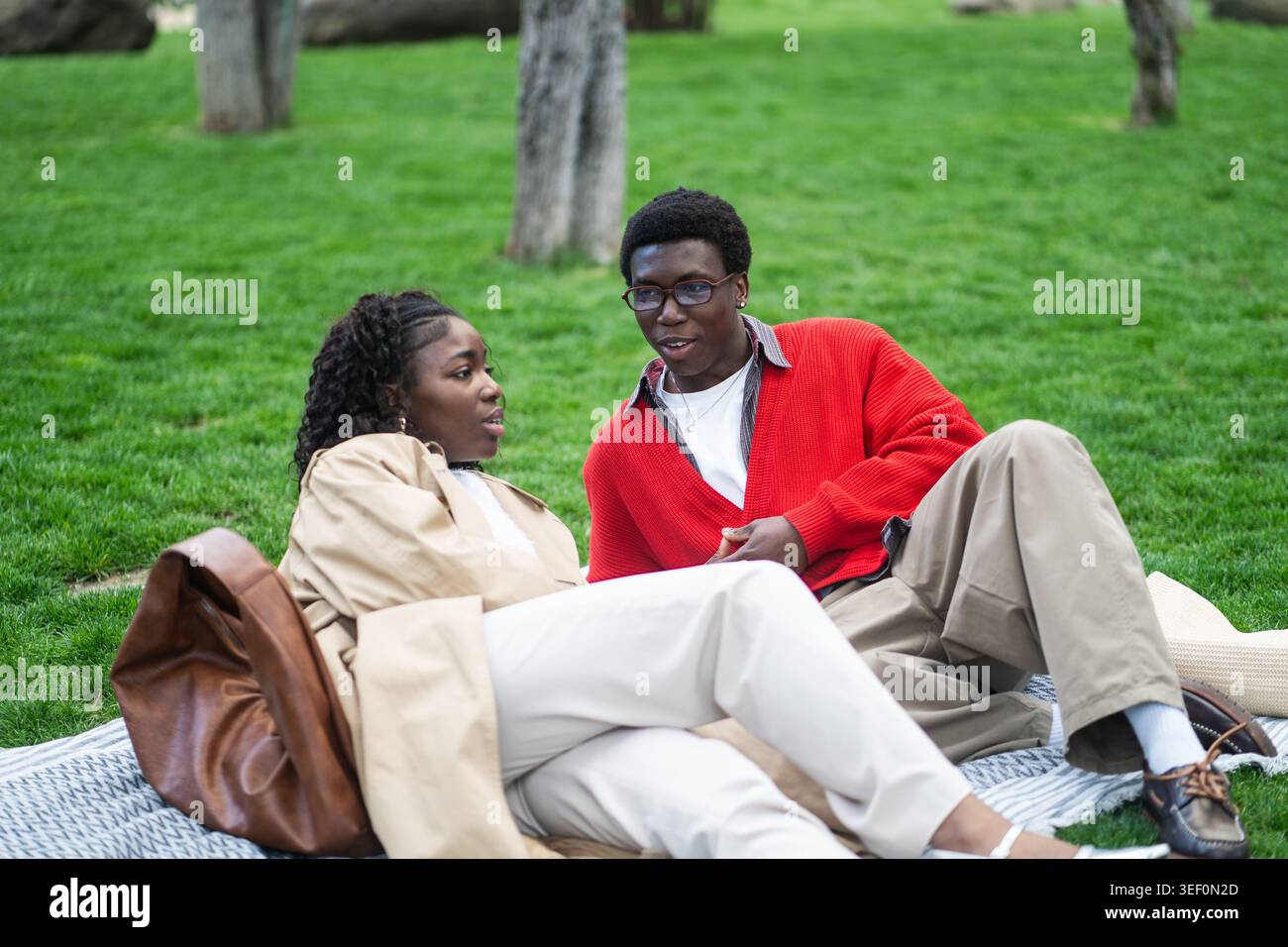 Positives afroamerikanisches Paar, Mann und Frau, die zusammen auf Karo im Stadtpark beim Picknick sitzen. Stockfoto