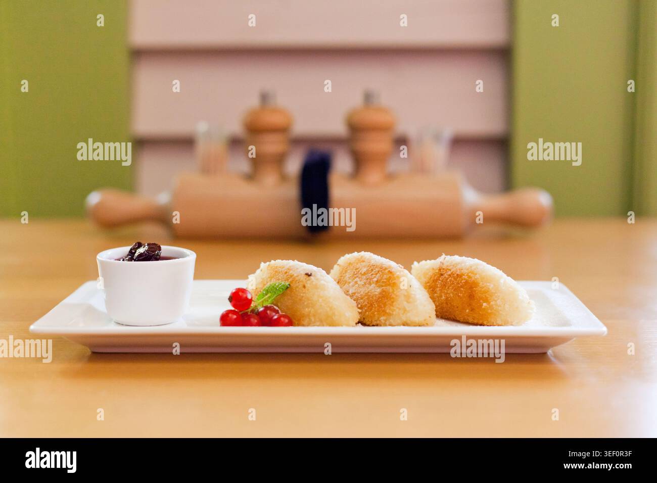 Gebratene Teigtaschen auf weißem Teller mit Beerenmarmelade und roten Johannisbeeren. Geringe Schärfentiefe mit verschwommenem Restauranthintergrund sorgt für warme, einladende Stimmung. Stockfoto