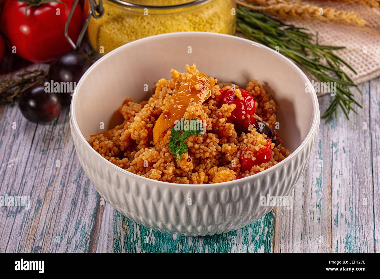 Nahaufnahme von köstlichem Couscous-Salat mit geröstetem Gemüse in weißer Keramikschale. Rustikales Ambiente mit Rohzutaten auf verwittertem blauen Holztisch Stockfoto