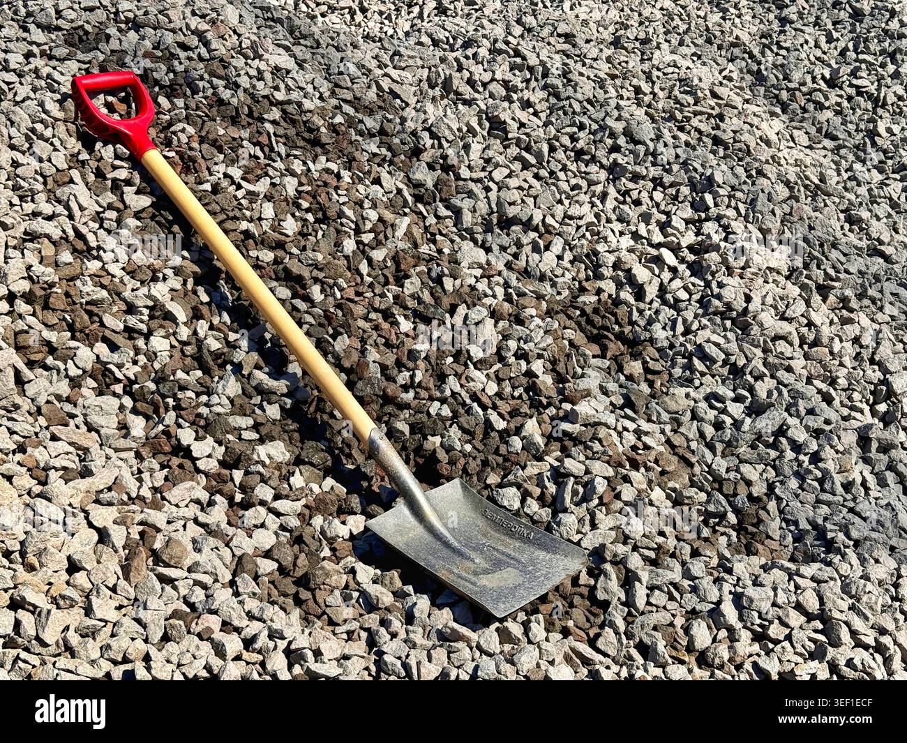 Eine quadratische Schaufel steht vor einem Haufen Schotter auf einer Baustelle im Freien Stockfoto