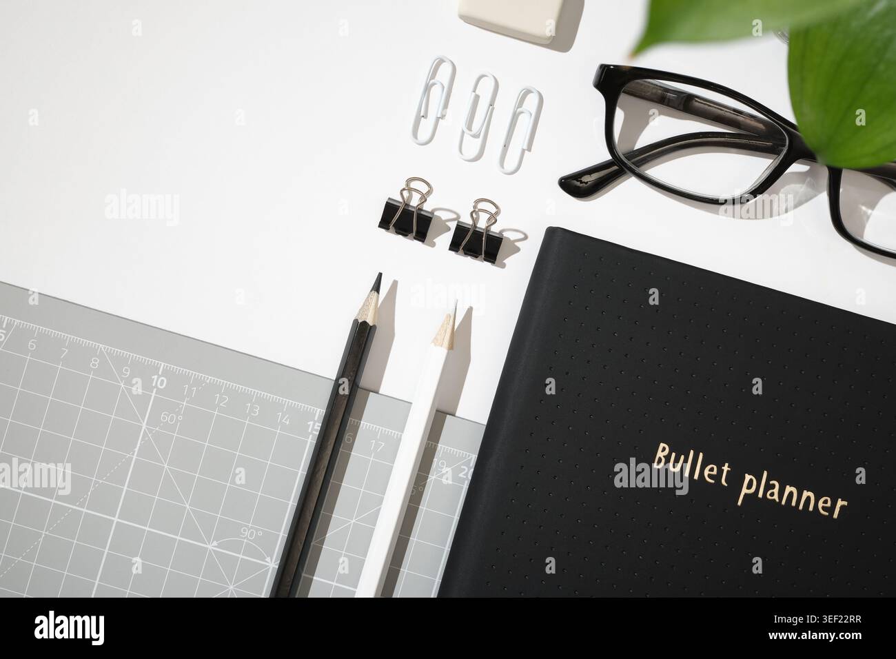 Flache Lage des schwarzen Planers mit Büroklammern, Binderklammern, Brille, Radiergummi und Schneidematte auf weißem Hintergrund. Kopierraum Stockfoto