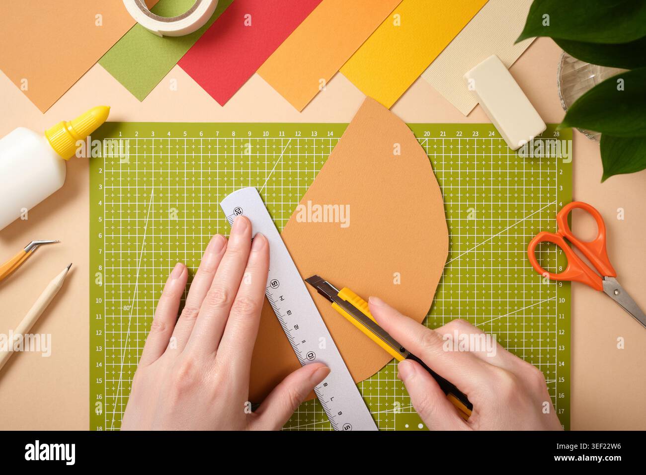 Hände mit einem Universalmesser und einem Lineal zum Schneiden von farbigem Papier auf einer grünen Schneidematte. Kreativer Arbeitsbereich mit Schere, Leim und Schreibwaren für Heimwerker Stockfoto