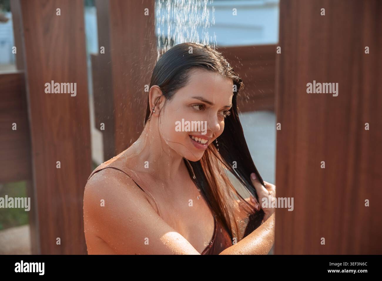 Attraktive Frau, die sich in der Nähe einer tropischen Badedusche mit glühender Sommerhaut entspannt. Porträt des weiblichen Modells, das erfrischendes Wasser und gesundes Aussehen genießt Stockfoto