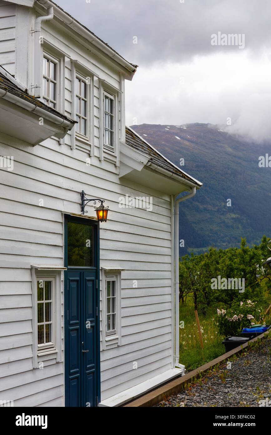 Nordisches lokales weißes Holzhaus neben Obstgarten und nebeligen Berghängen in Lofthus Norwegen, das die ruhige Fjordroutine für Skandinavi widerspiegelt Stockfoto