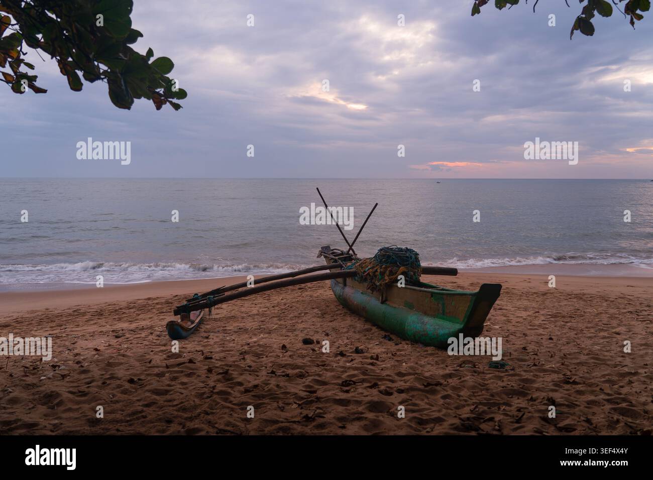 Traditionelles Auslegerboot parkt am Sandstrand von Tangalle bei Sonnenuntergang unter bewölktem Himmel in der Südprovinz Sri Lanka Stockfoto