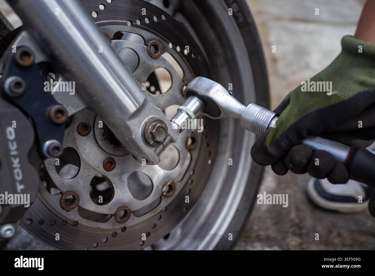 Nahaufnahme mit Handschuhen zur Prüfung von Bremsscheibe und Bremssattel, Positionierung der Bremsbeläge sichtbar, metallische Textur Stockfoto