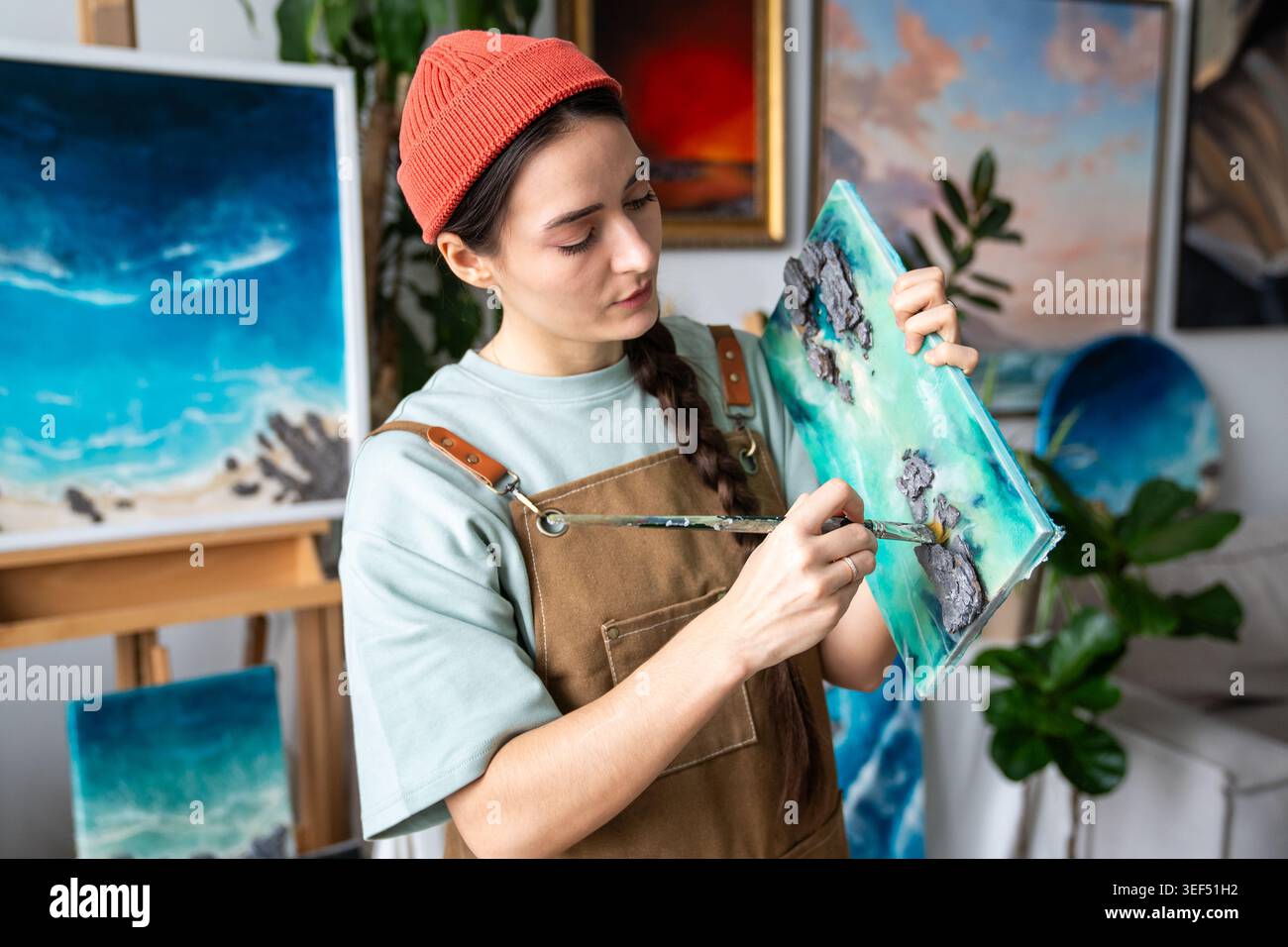 Geschickte Frau, die Leinwand mit fertiger flüssiger Kunstmalerei hält und Staub von Kunstwerken entfernt. Stockfoto