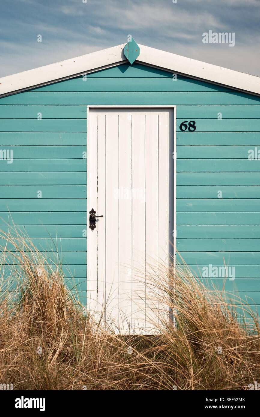 Eine helle türkisfarbene hölzerne Strandhütte mit einer einzigen weißen Tür auf einer grasbewachsenen Sanddünenbank in Hunstanton, Norfolk, England Stockfoto