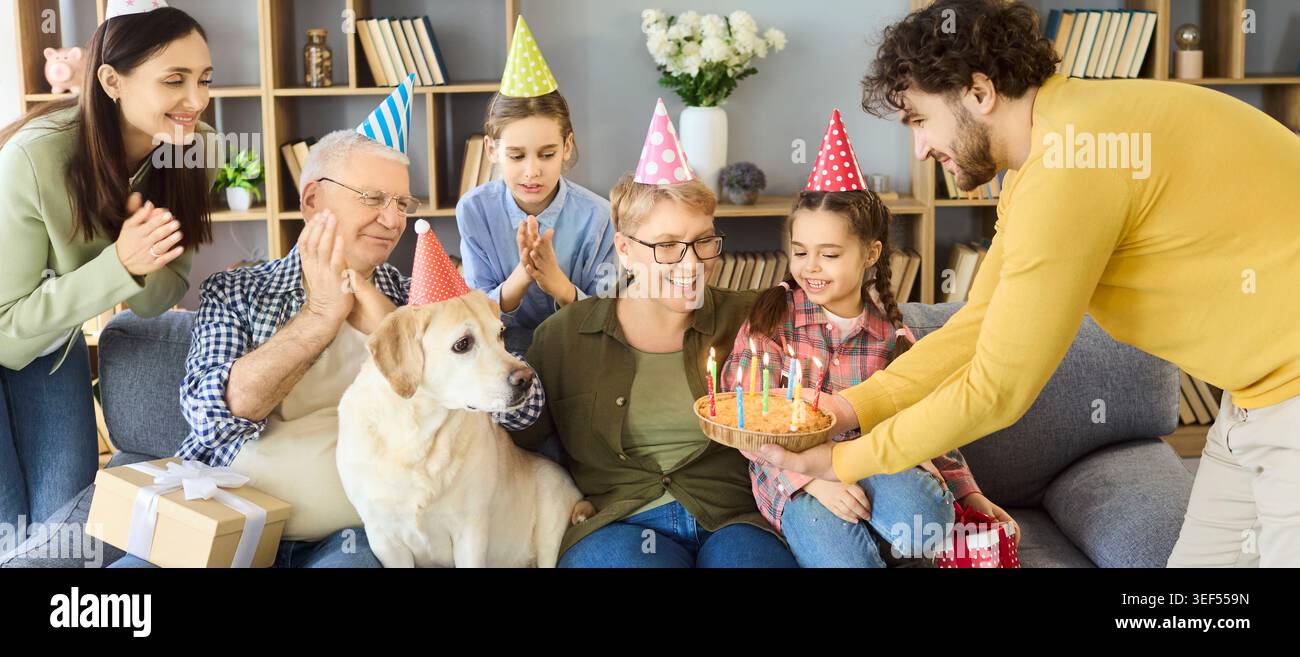 Glückliche Familie, die zu Hause Geburtstag mit Kuchenkerzen und Labrador-Hund feiert Stockfoto