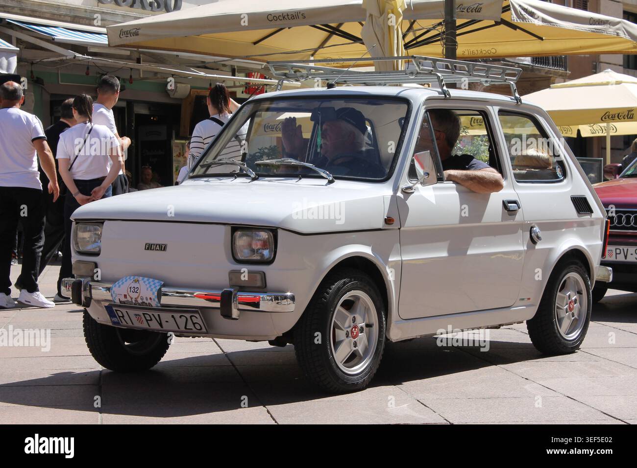 Kleiner weißer Fiat 126p mit Dachträger, der während der 30. Internationalen Oldtimer Auto Rallye in Rijeka, Kroatien, am 2. Mai 2026 an Cafés vorbeifährt. Stockfoto