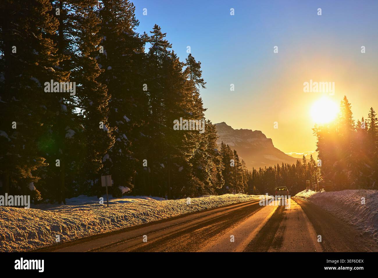 Winter Road Sonnenaufgang im verschneiten Kiefernwald mit Blick auf die Berge Stockfoto