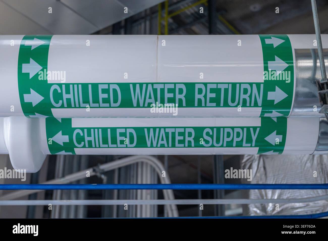 Gekennzeichnete Kühlwasserversorgungs- und -Rücklaufleitungen führen durch einen industriellen Maschinenraum und zeigen Richtungsmarkierungen auf isolierten HLK-Leitungen. Stockfoto