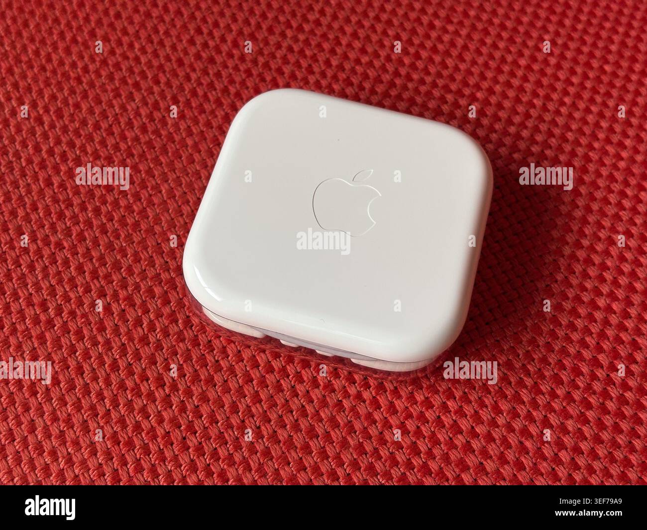 Ein kleines weißes Apple-Gerät mit dem Apple-Logo befindet sich auf einer roten gewebten Stoffoberfläche. Stockfoto
