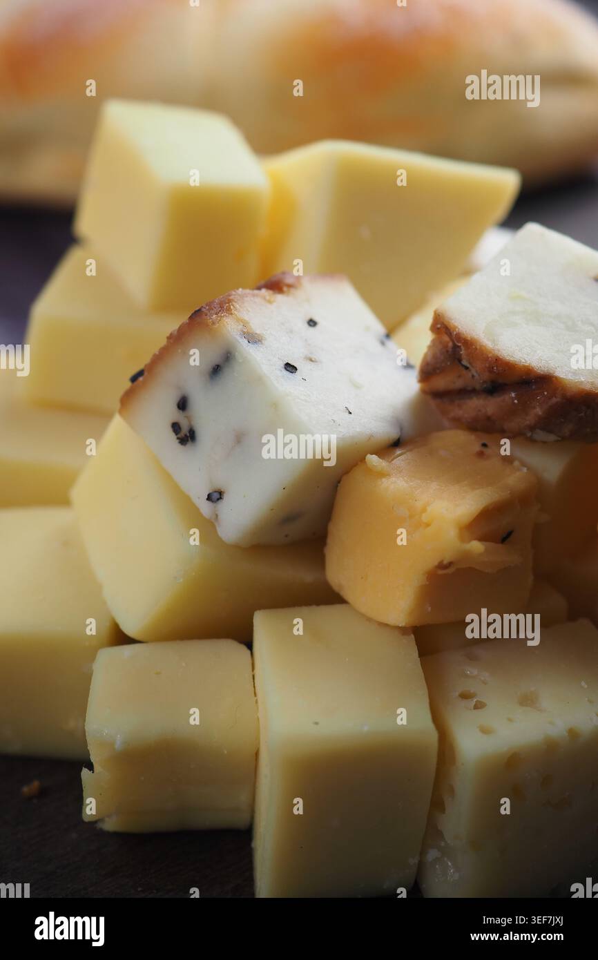 Käsewürfel auf einem Holzbrett mit Brot im Hintergrund Stockfoto
