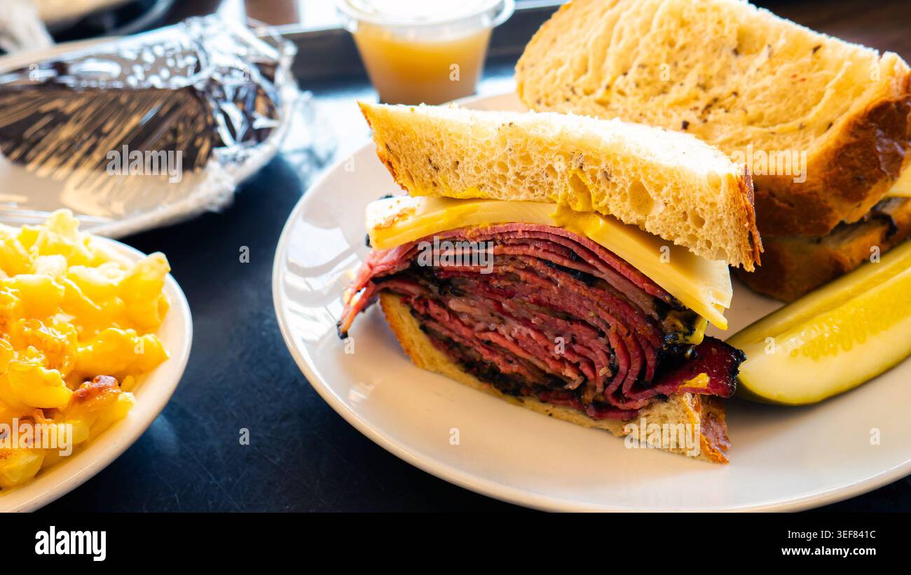 Pastrami Sandwich, Pastrami auf Roggen mit Schweizer Käse und Senf, serviert mit Gurke, Makkaroni und Käse in einem New Yorker Feinkostgeschäft Stockfoto