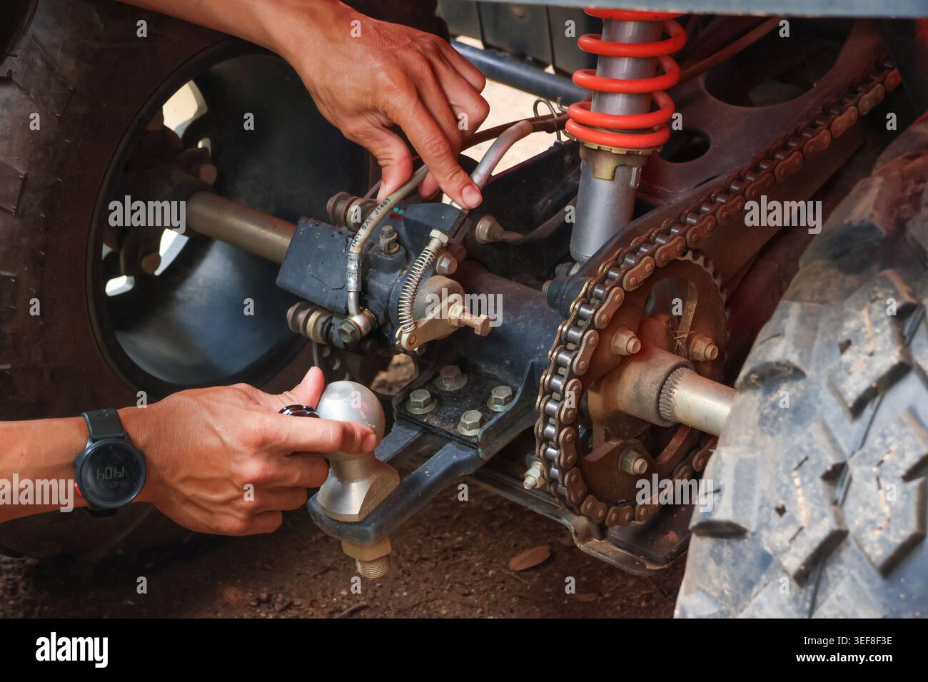 Fokussierter Mechaniker, der sorgfältige Reparaturen an einem Geländewagen-atv-Aufhängungssystem durchführt, das die Metallkette und Hinterachse mit einer fettigen Hand neben dem Gummilager anpasst Stockfoto