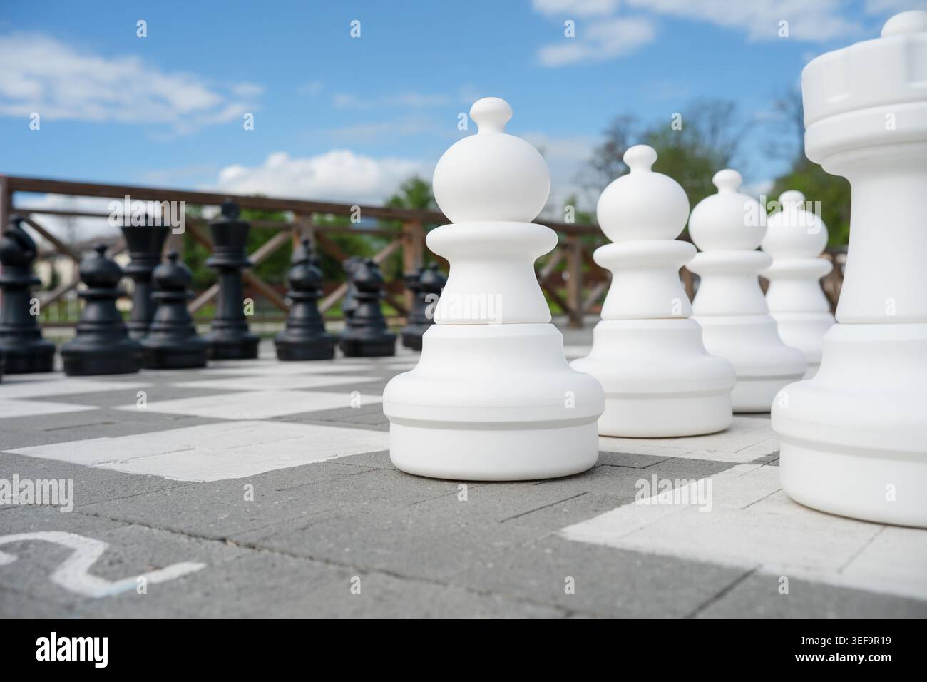 Nahaufnahme eines riesigen Plastikpfandstücks auf einem großen Schachbrett im Freien unter klarem blauen Himmel, Unternehmensgründung und Strategiekonzept. Stockfoto