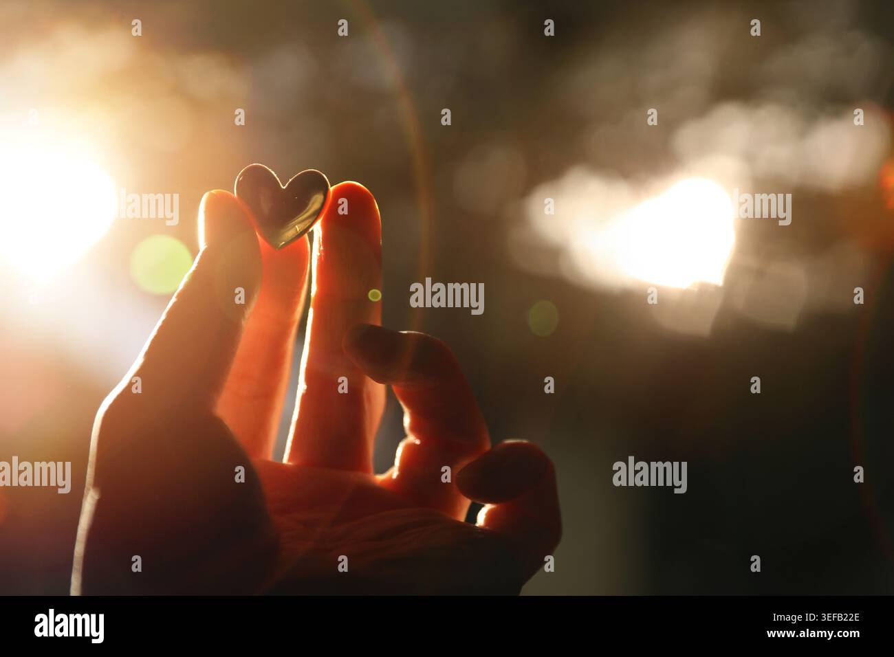 Ein romantisches Konzept, das Liebe und Aufregung vor einem leuchtenden Herzhintergrund und Fingerspitzen mit einem kleinen goldenen Herz ausdrückt. Stockfoto