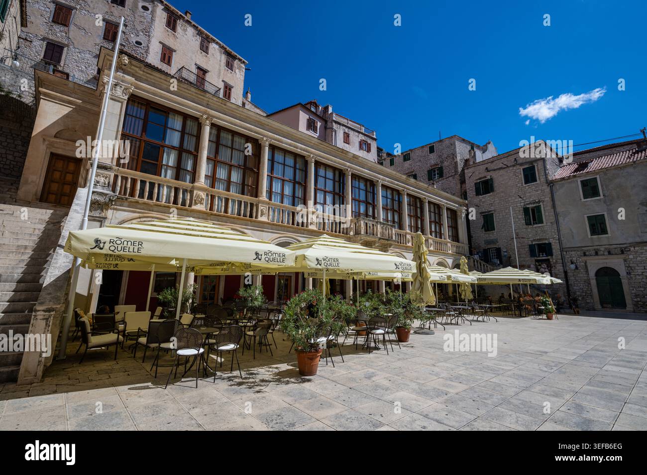 An einem sonnigen Tag gibt es einen Essbereich im Freien mit Sonnenschirmen in der Nähe historischer Gebäude in Sibenik Kroatien Stockfoto
