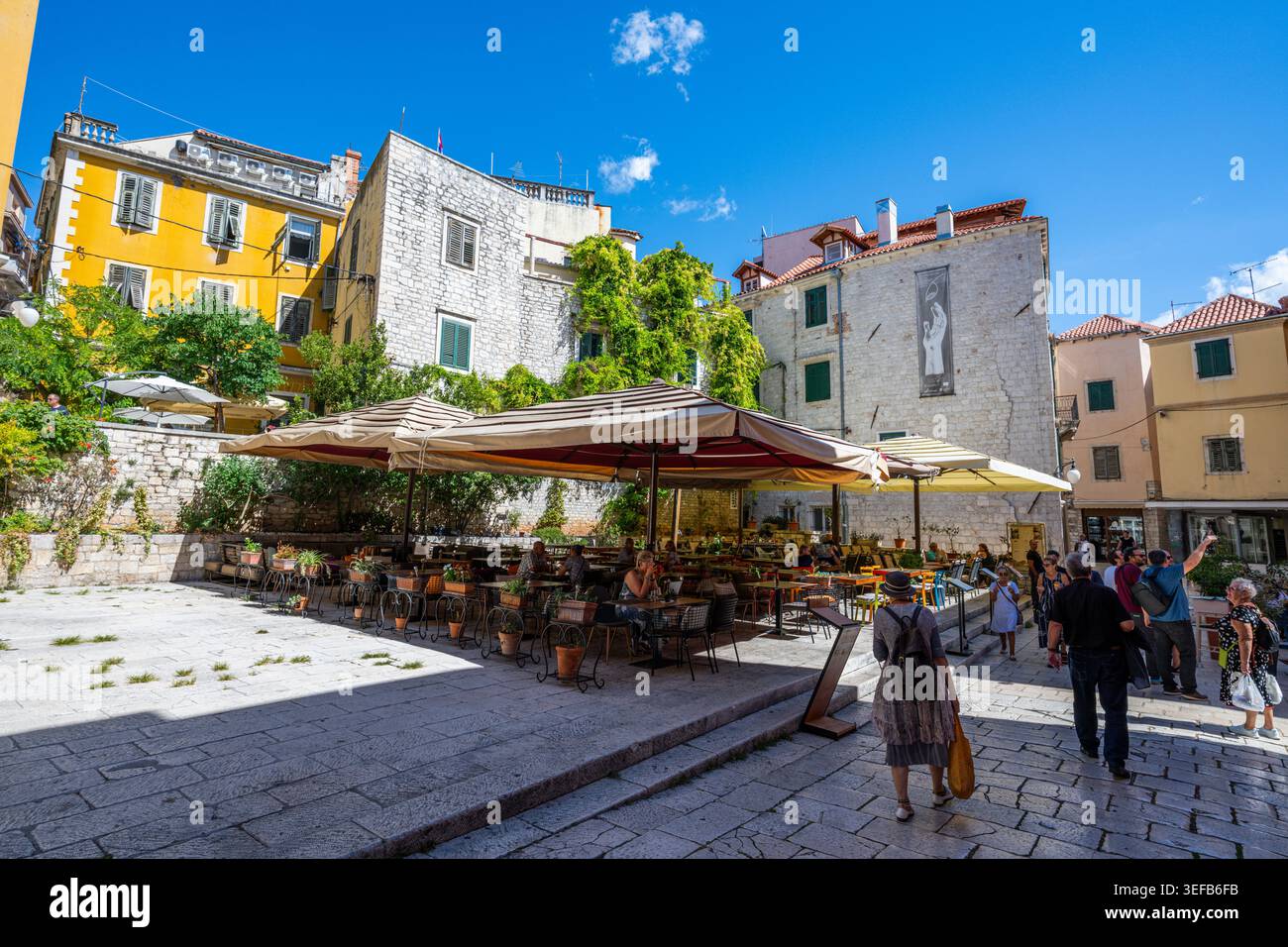 Sonnendurchfluteter Platz in der Altstadt mit Sitzplätzen im Freien und Besuchern in Sibenik, Kroatien Stockfoto