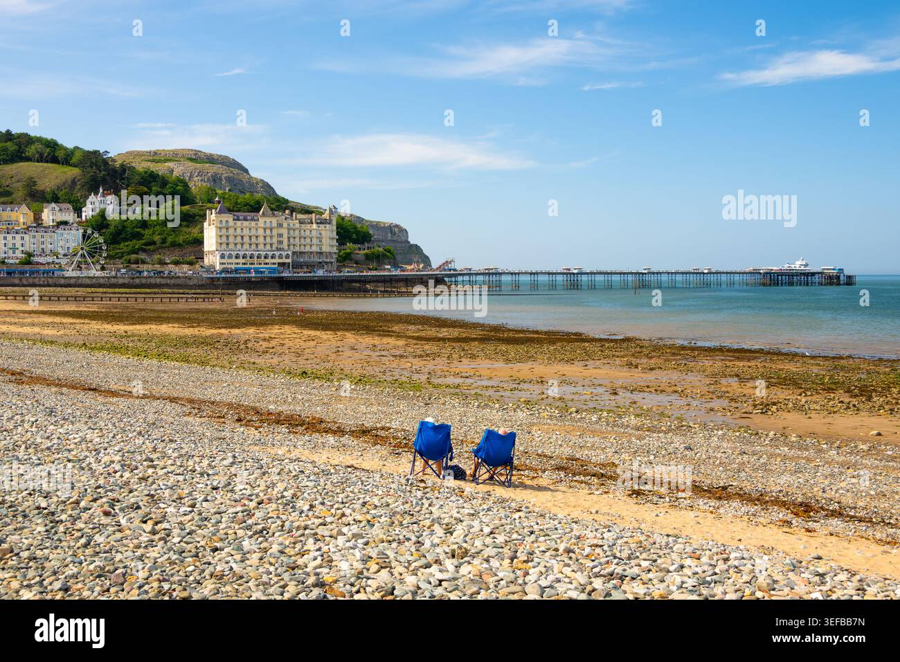 Paare genießen einen sonnigen Tag am Strand von Llandudno mit Pier und Landschaft im Hintergrund, Conwy, Wales Stockfoto