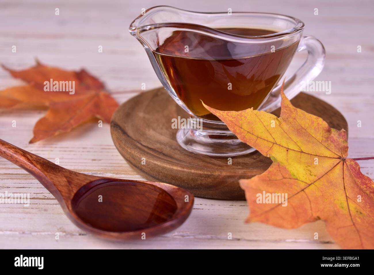 Ahornsirup in einem Glas Soße Boot und Ahornblätter. Stockfoto