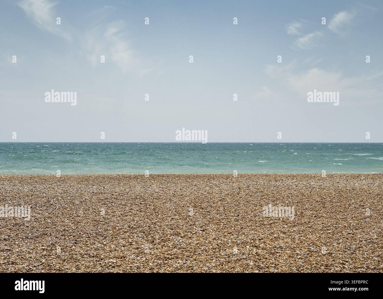Weite Panoramaaussicht auf einen leeren Sandstrand, der auf ein ruhiges blaues Meer unter hellem Himmel an der Küste von Brighton trifft. Stockfoto