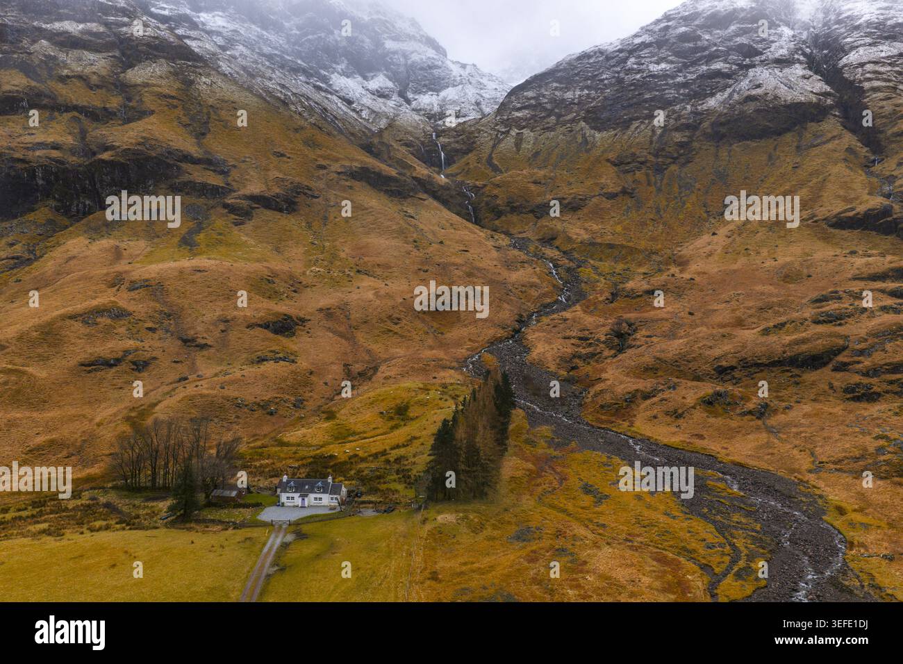 Aus der Vogelperspektive eines weißen Häuschens am Fuße der schneebedeckten Berge in Glencoe, Schottland, Großbritannien. Stockfoto