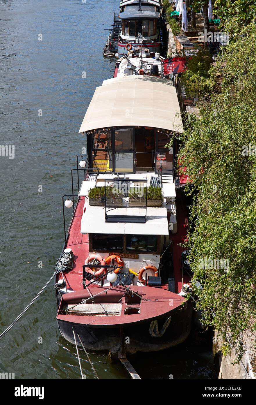 Paris, Frankreich - 11. Mai 2026: Das historische Binnenschiff Peniche Le Marcounet legt an der seine an, mit üppigem Grün und zusätzlichen Booten im Hintergrund Stockfoto
