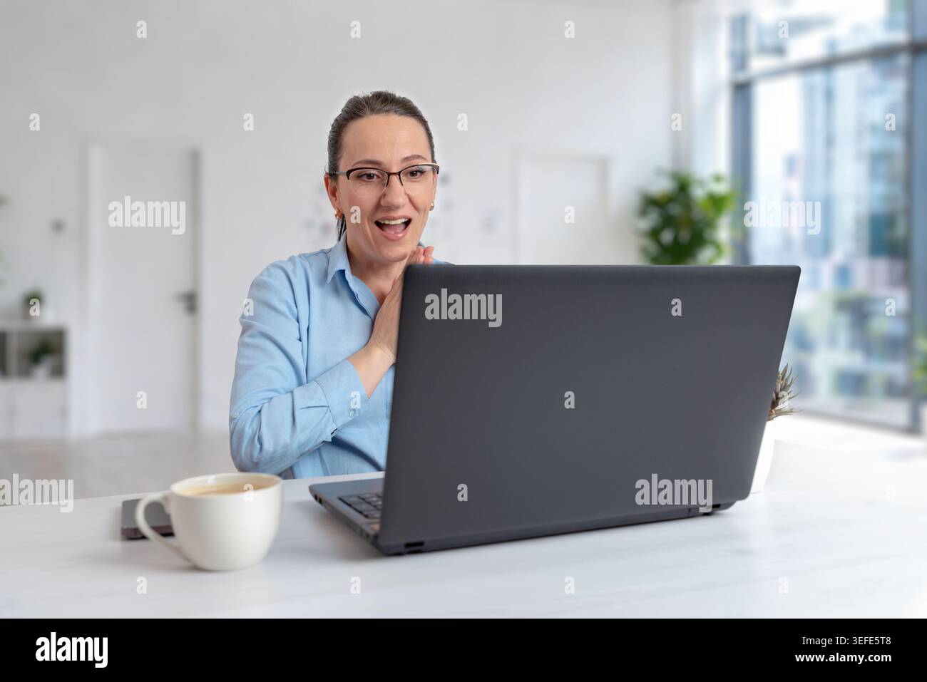 Begeisterte Frau, die während eines Remote-Meetings oder eines Online-Erfolgs auf ein Notebook reagiert und positive Geschäftskommunikation und modernen Arbeitsstil erfasst Stockfoto