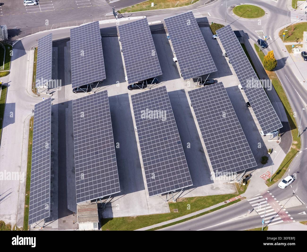 Luftaufnahme von Solarpaneelen, die über einem Parkplatz mit geparkten Autos und städtischer Infrastruktur in Slowenien installiert sind. Stockfoto