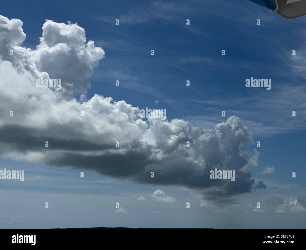 Eine weite Aufnahme eines tiefblauen Himmels, gefüllt mit dramatischen, dicken weißen Kumuluswolken über dem Ozeanhorizont. Stockfoto