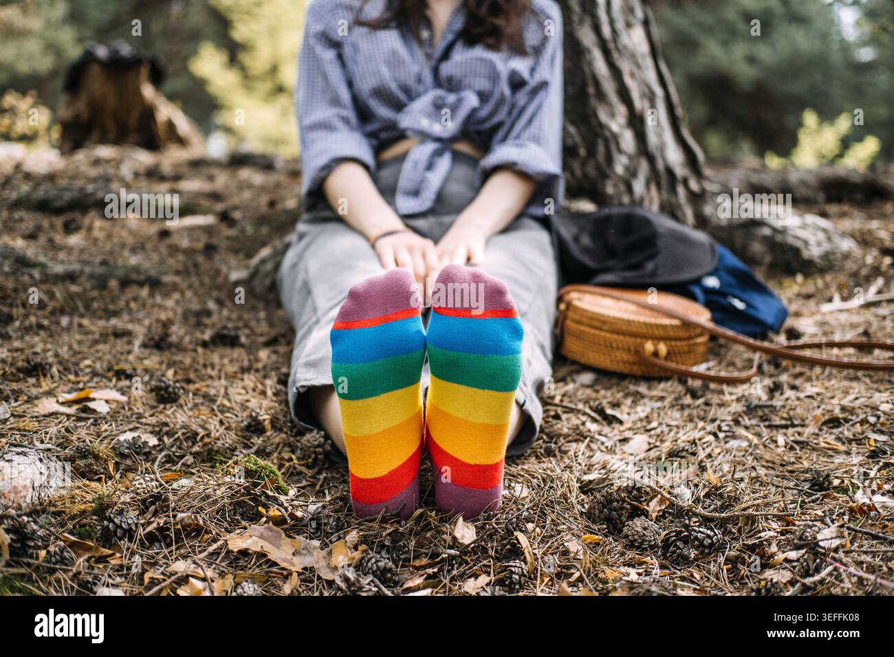 Die Person sitzt mit den Händen auf den Füßen auf dem Waldboden und trägt Regenbogensocken. Authentische Selbstdarstellung, ruhiger Stolz, alltägliches lgbt-Leben. Stockfoto