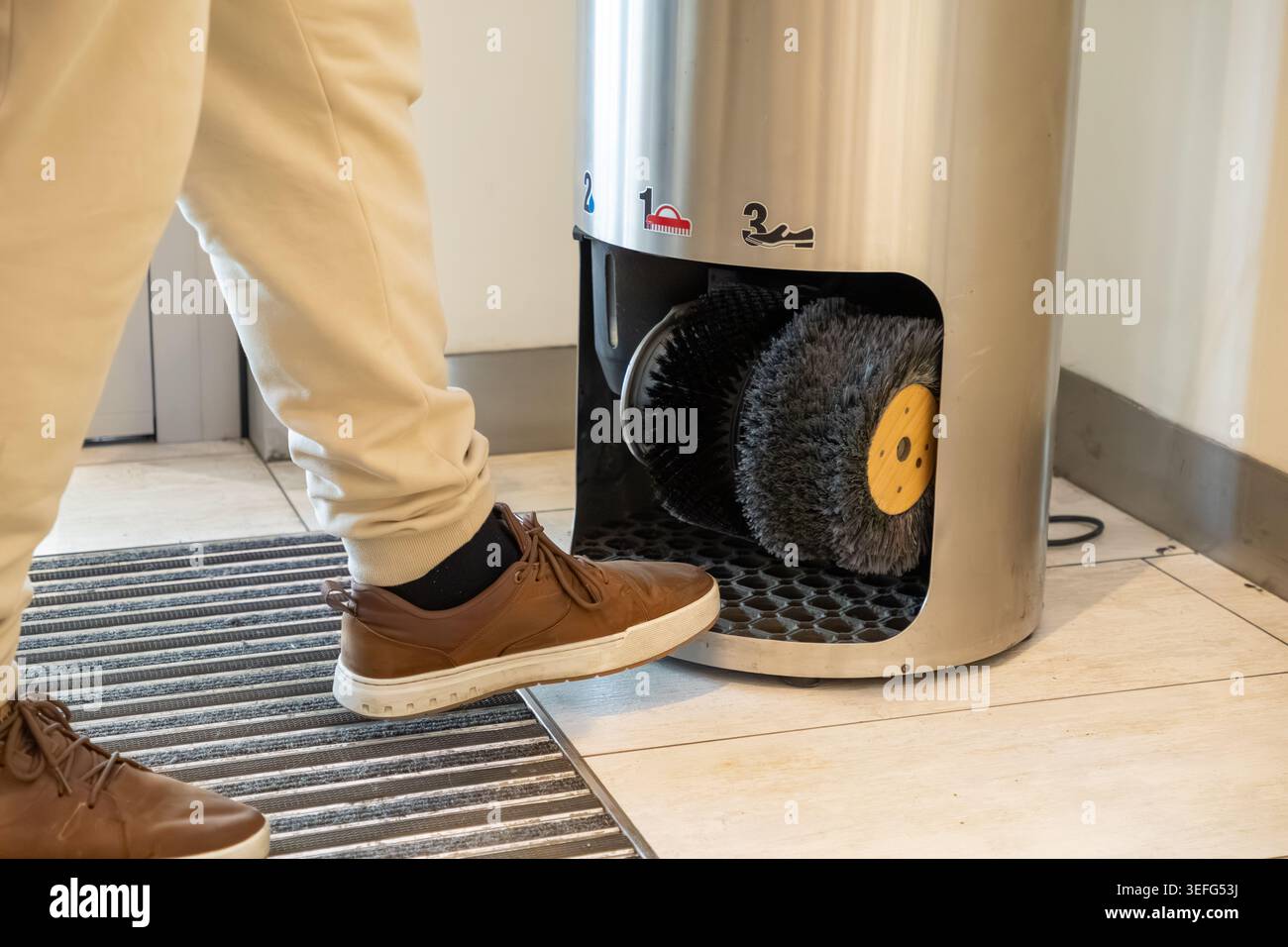 Eine Nahansicht zeigt eine Person, die einen Lederschuh in ein elektrisches Poliergerät mit motorisierten Bürsten legt, um Schuhe effizient und hochgradig zu reinigen Stockfoto