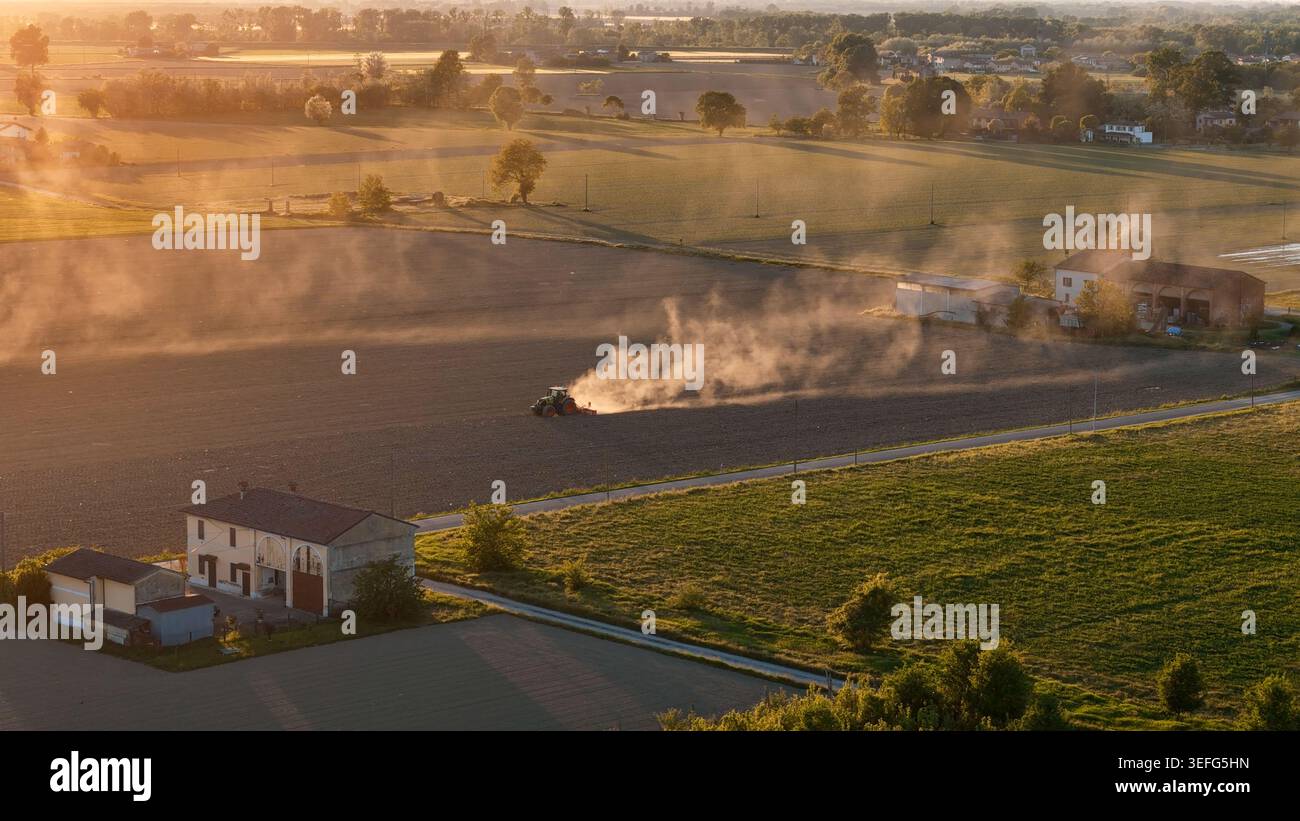 Traktor bewirtschaftet trockenen Boden und schleudert Staub bei Sonnenuntergang Stockfoto