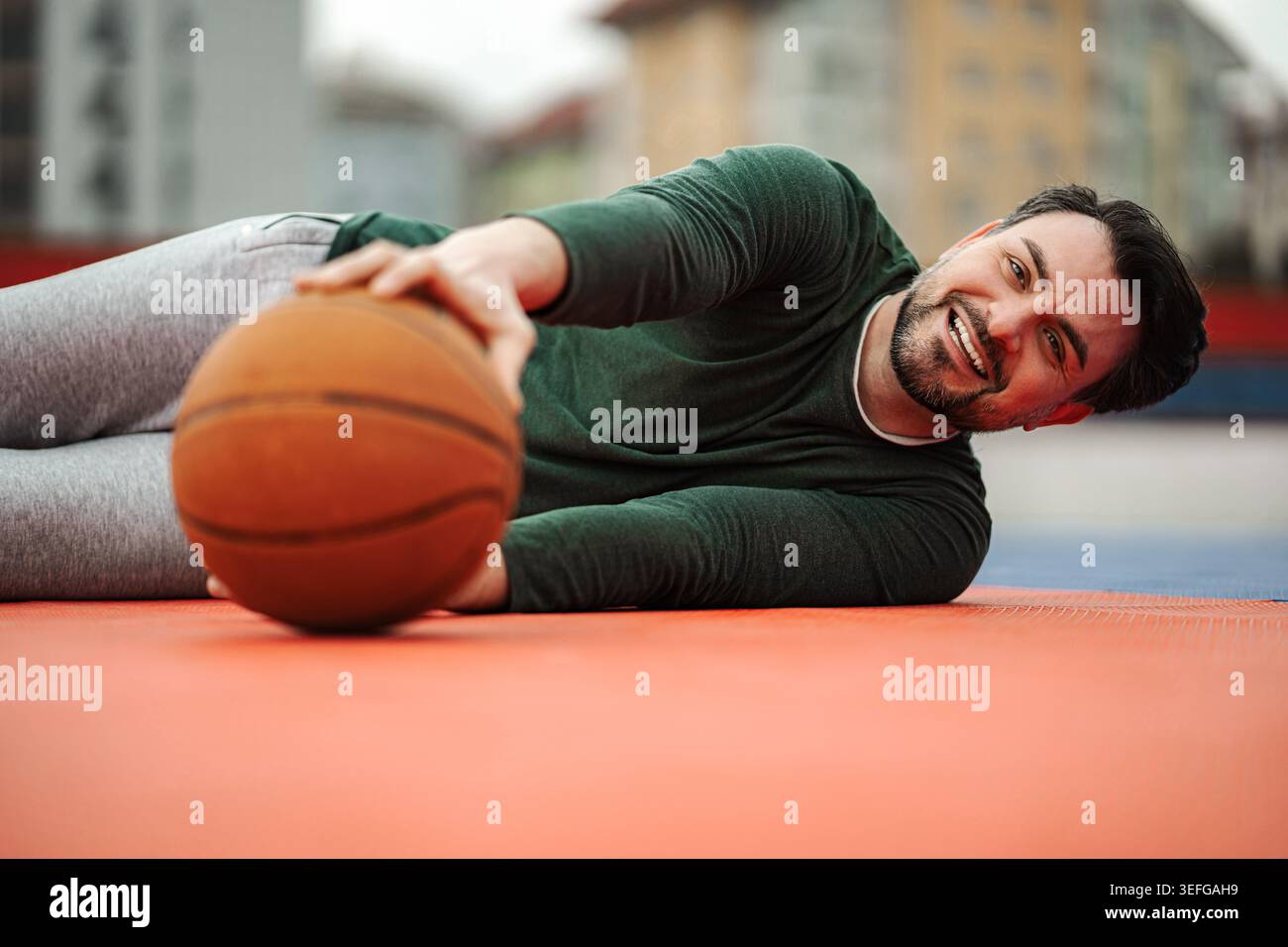 Lügender Mann auf dem Basketballfeld lächelnd mit Ball Stockfoto